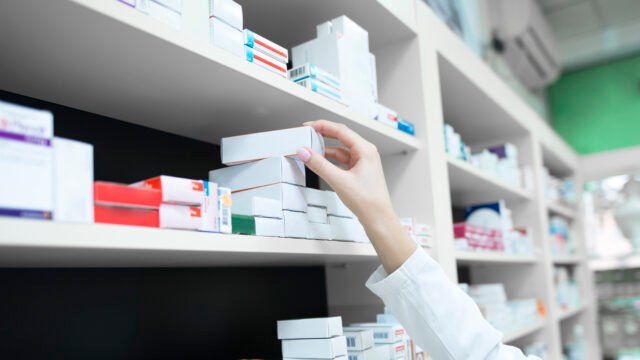 Closeup view of pharmacist hand taking medicine box from the shelf in drug store.